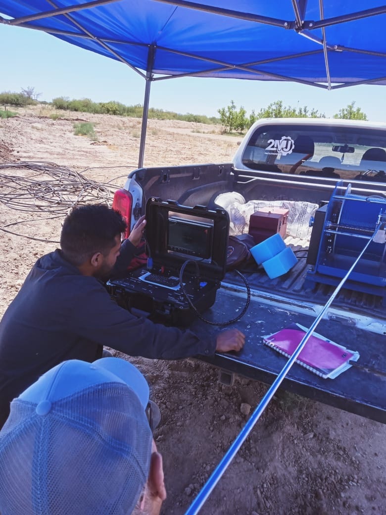 Técnico 2MJ operando equipo de diagnóstico en campo bajo carpa azul, camioneta con logo 2MJ